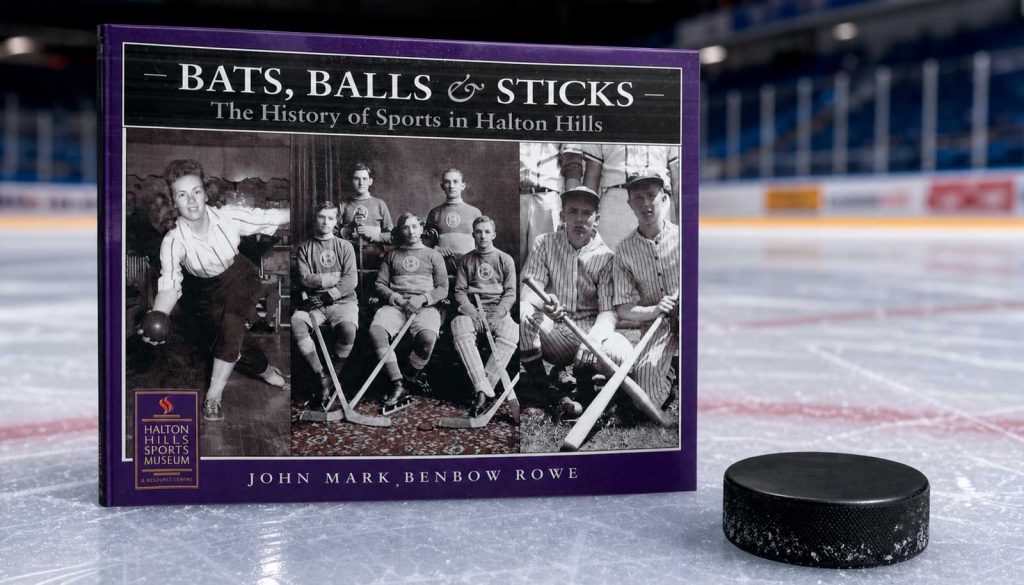 Purple book cover titled 'Bats, Balls & Sticks: The History of Sports in Halton Hills' on an ice rink beside a black hockey puck.