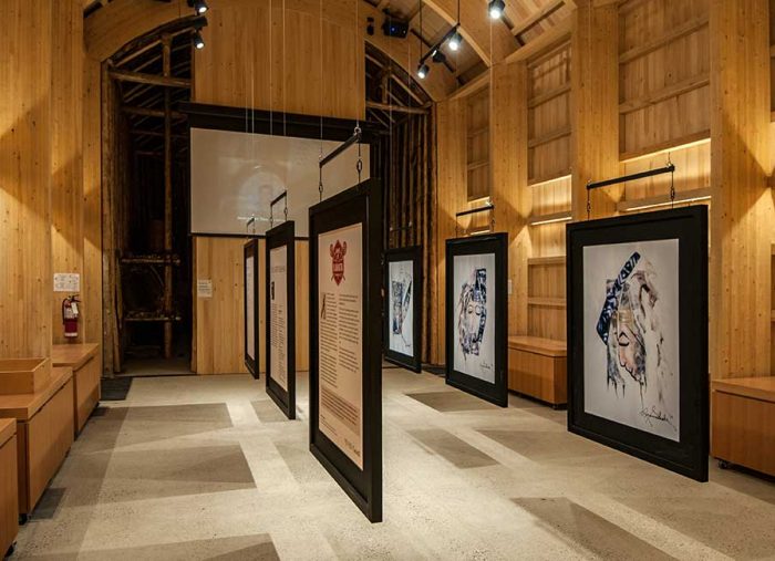 Wood-paneled gallery with large hanging framed artworks displayed along a central aisle. (Informative)