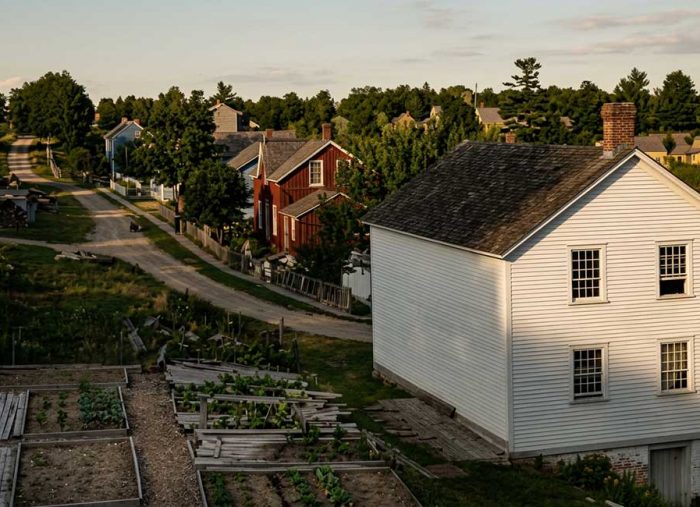 Limehouse village. 1891. White two-story wooden house with a pitched roof overlooking raised vegetable gardens and a winding dirt road in a small rural town.
